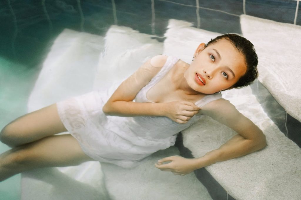 Asian woman in a white dress lounging in a swimming pool, serene and elegant.