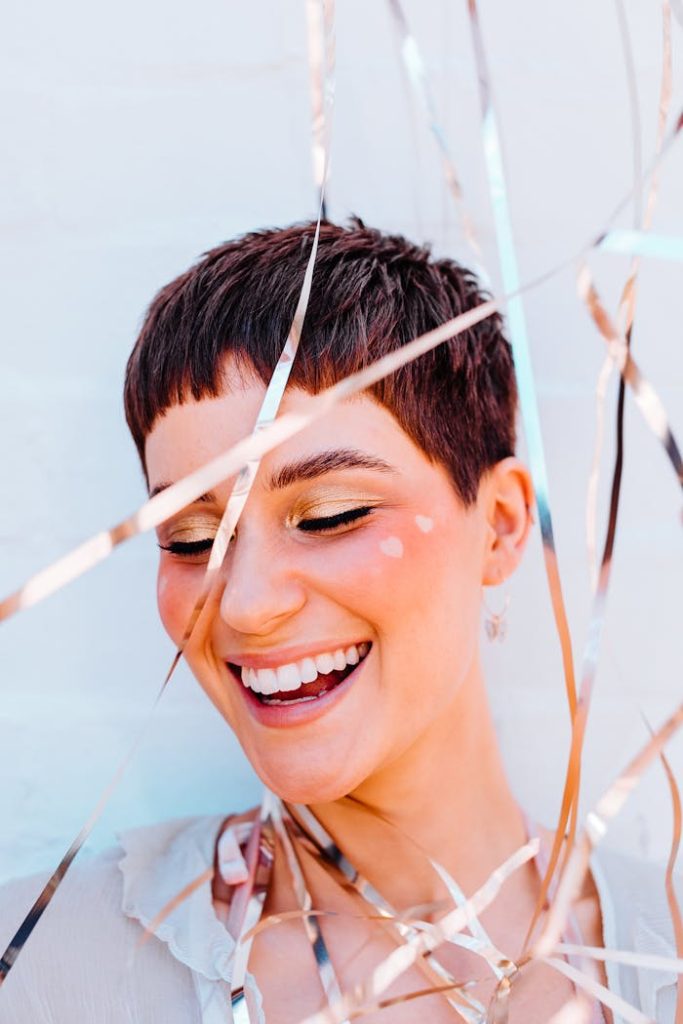 A cheerful woman with short hair smiling joyfully surrounded by vibrant ribbons.